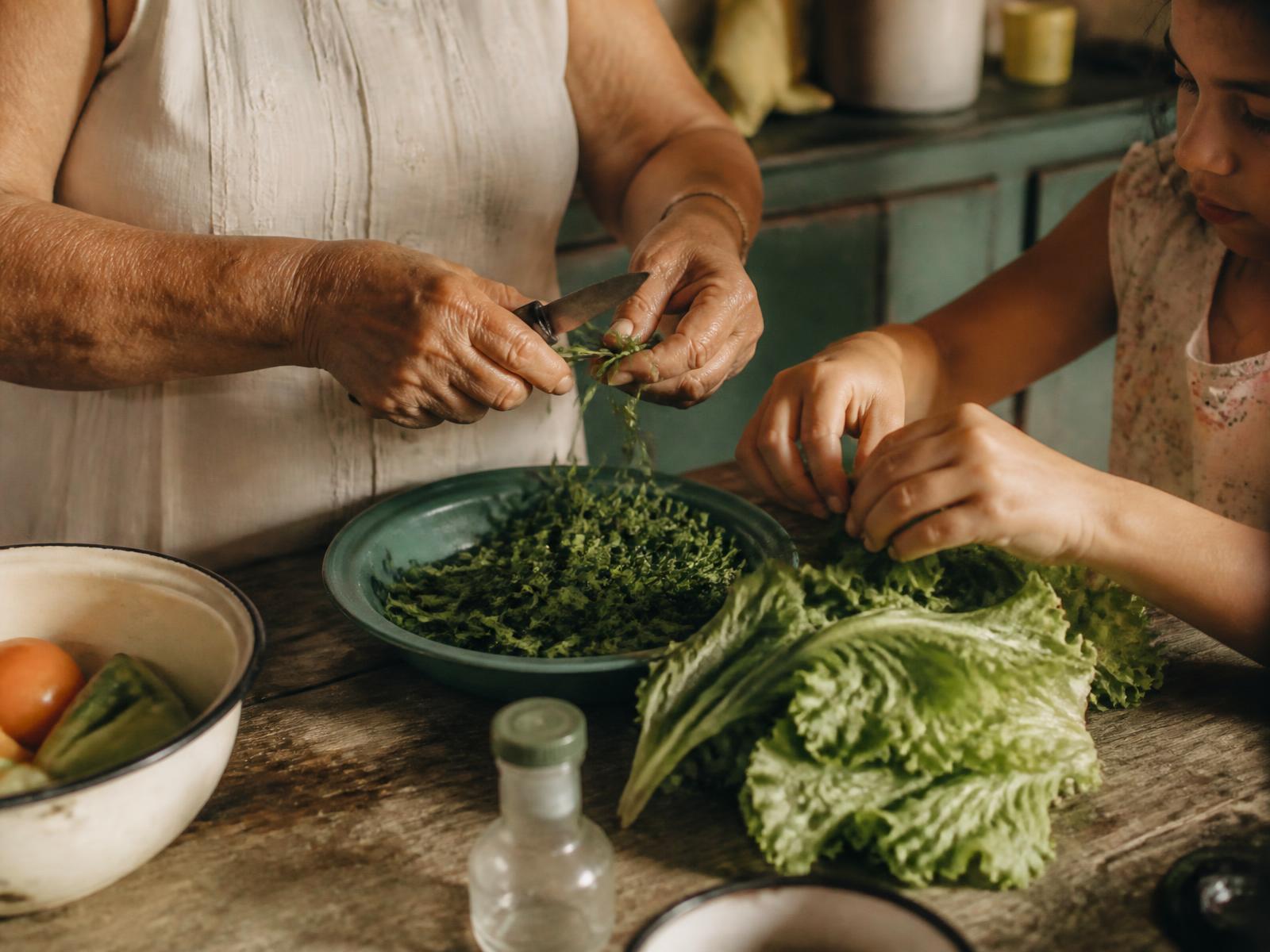 Mãos de uma avó e de uma criança preparando verduras frescas em uma mesa de madeira